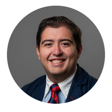 Man of hispanic descent with short dark hair wearing a blue suit jacket and tie