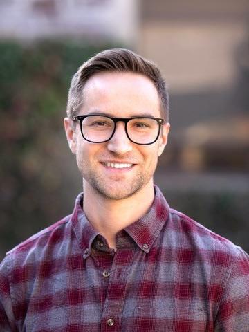 White man with short light brown hair wearing glasses and a maroon and purple plaid shirt